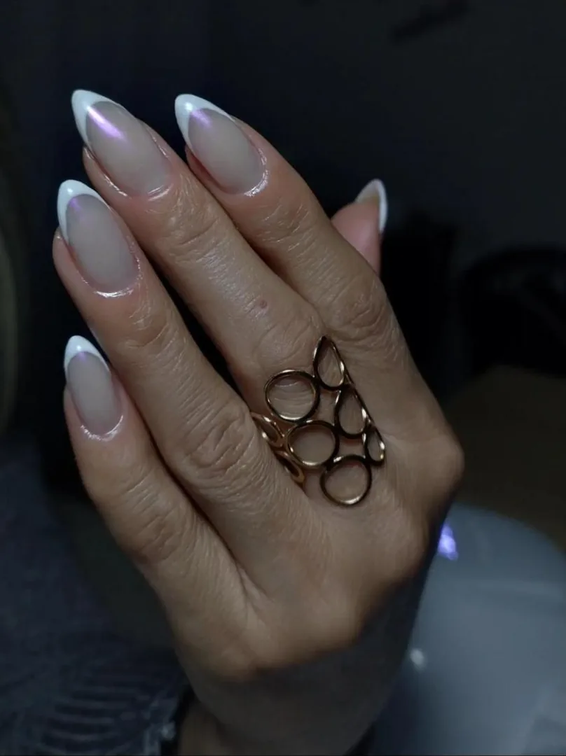 Mão com unhas alongadas amendoadas, francesinha branca com brilho perolado e anel dourado